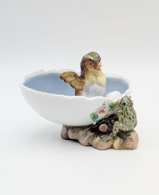 un petit oiseau perché dans un bol sur lequel est représentée une grenouille