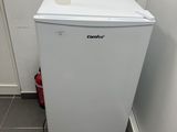 un petit réfrigérateur blanc dans le coin d'une pièce