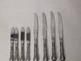 six silverplated knives and six knives are lined up on a white surface