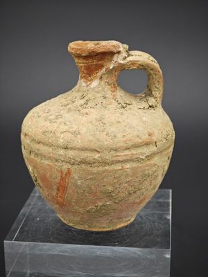 un vieux vase muni d'une anse, posé sur un socle transparent