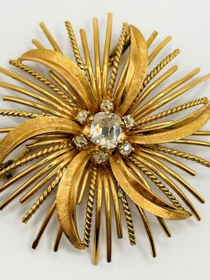 an image of a gold flower brooch with a crystal center
