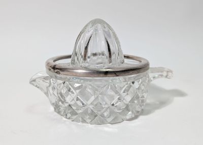 un presse-agrumes en verre avec un couvercle argenté, posé sur une surface blanche