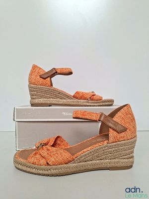 une photo représentant une paire de sandales à talons compensés orange posée sur une boîte