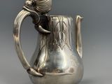 un pichet ancien en argent orné d'une fleur sur l'anse