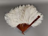 a white ostrich fan with a wooden handle on a gray surface