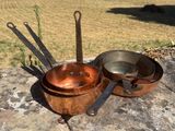 des casseroles et des poêles posées sur un rocher, avec un champ en arrière-plan