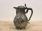 a silver pitcher on a wooden table with a white wall in the background