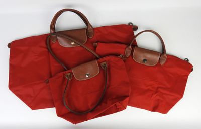 trois sacs rouges avec des anses marron, posés sur un fond blanc