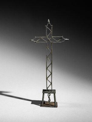 a metal cross on a stand with a shadow on the ground
