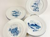 quatre assiettes bleues et blanches ornées de motifs de poissons sur fond blanc