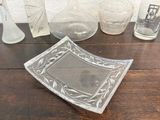 a glass plate sitting on a wooden table next to a glass vase
