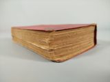 an old book with a red cover sitting on a white surface