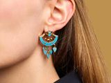 a woman wearing a pair of earrings with turquoise and gold details