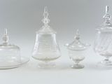 three clear glass containers with lids and a saucer on a white surface