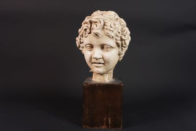 un gros plan sur la tête d'un enfant sculptée dans la pierre, posée sur un socle en bois