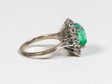 a close up of an emerald and diamond ring on a white surface