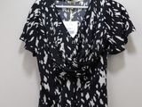 the top of a black and white blouse with white spots is hanging on a hanger