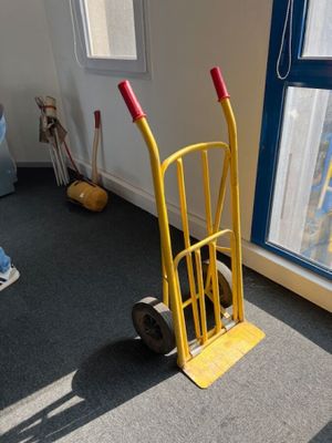 un diable jaune avec une poignée rouge, près d'une fenêtre