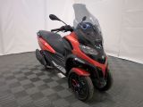 une photo d'une moto rouge et noire garée sur un sol à damier