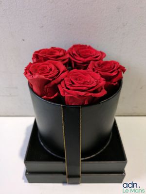 des roses rouges dans une boîte noire posée sur une table blanche