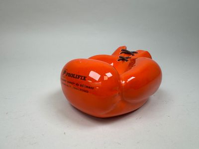 une pomme orange en forme de citrouille posée sur une surface blanche