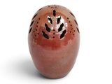 un vase rouge percé de trous posé sur une surface blanche