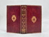 an old red book with gold trim sitting on a white surface