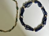 a blue beaded necklace and a gold necklace on a white surface