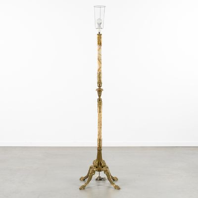 un grand lampadaire en métal doré surmonté d'un abat-jour en verre