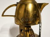 une théière en laiton posée sur un support, sur une surface blanche