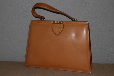 un sac à main en cuir marron posé sur une table devant un mur gris