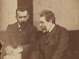 trois hommes assis à une table, dont l'un est en train de couper un gâteau