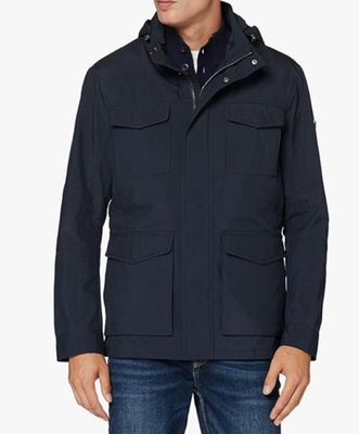 un homme vêtu d'une veste et d'un jean, debout devant un fond blanc