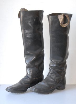 pair of black leather boots on white surface with white wall in background