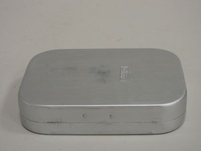 une petite boîte métallique avec un couvercle, posée sur une surface blanche