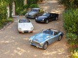 three classic cars parked in a driveway next to trees and bushes