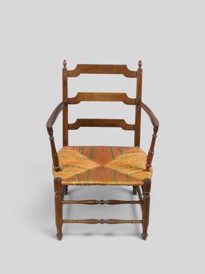 une vieille chaise en bois dont l'assise est jaune et rouge sur fond gris