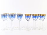 six verres à vin bleus et dorés alignés sur une surface blanche