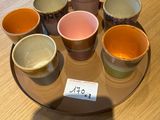 six tasses de couleurs différentes posées sur une assiette, sur une table
