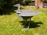 a metal sculpture of a duck on a stand in the grass