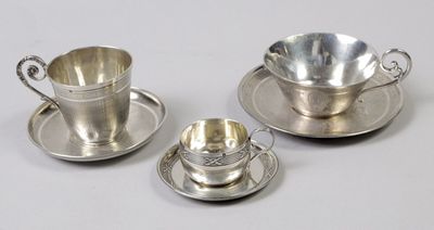 trois tasses à thé en argent avec leurs soucoupes, posées sur une surface blanche