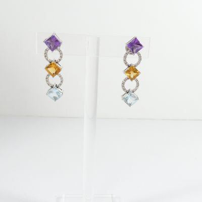 a pair of earrings with multi colored stones on a stand
