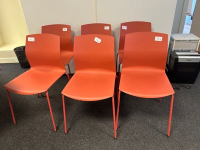 four orange plastic chairs are lined up in a row