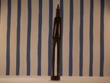 a statue of a man standing on a table in front of a striped wall