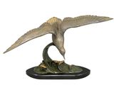 sculpture en bronze représentant un oiseau posé sur un socle feuillu, sur fond blanc