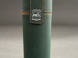 the green cylinder is holding a leather case with a logo on it