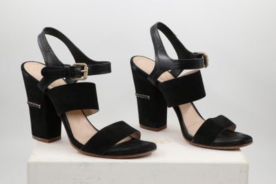 une paire de sandales noires à talons hauts posée sur un socle blanc