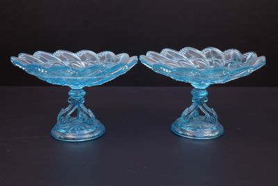 paire de plats en verre bleu reposant sur des socles, posés sur un support noir