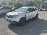La Dacia blanche est garée sur un parking, à côté d'autres voitures.