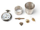 a silver cup, a pocket watch, a ring, and other items on a white surface